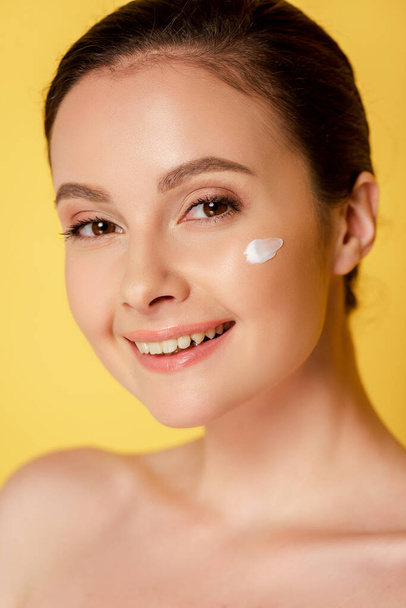 smiling naked beautiful woman with cosmetic cream on face isolated on yellow - Photo, Image