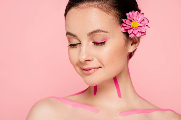 smiling naked beautiful woman with pink lines on body and flower in hair isolated on pink - Foto, afbeelding