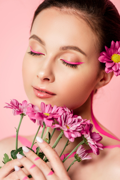 naked beautiful woman with closed eyes, pink lines on body and flower in hair holding bouquet isolated on pink - Fotó, kép