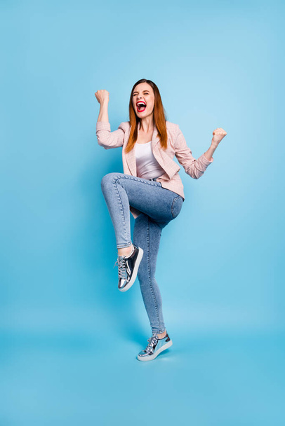 Full length photo of delighted crazy girl enjoy corona virus pandemic triumph win raise fists scream yeah wear good look clothes gumshoes isolated over blue color background - Valokuva, kuva