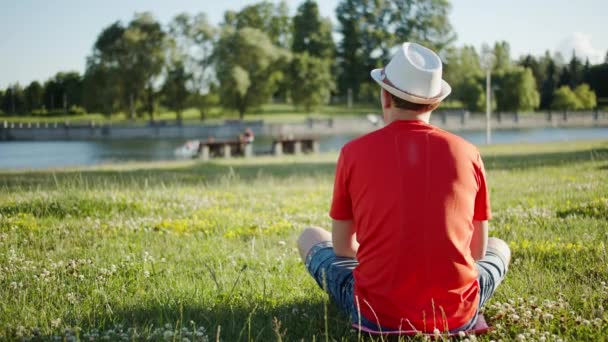 Egy kalapos férfi ül a természetben egy napsütéses napon, visszapillantás, nyár. - Felvétel, videó