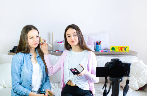 Dos chicas lindas blogger de belleza presentando productos cosméticos de belleza y transmitiendo video en vivo a la red social. Concéntrate en la bloguera influencer de chicas adolescentes. Belleza blogger y vlog concepto para adolescentes seguidores
. - Foto, imagen