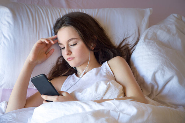 Adolescente utilisant un téléphone portable au réveil se sent bien le matin sur le lit - Photo, image