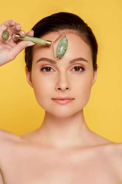 beautiful naked woman using jade roller on face isolated on yellow - Fotoğraf, Görsel