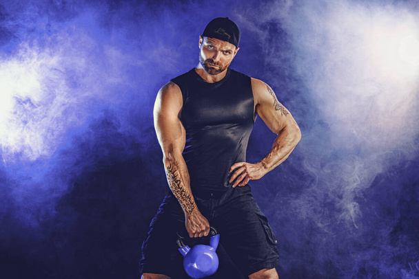Aggressive bearded muscular bodybuilder doing Exercise for the biceps with kettlebell. Studio shot - Foto, Imagen