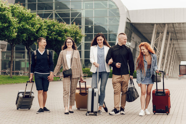 Glückliche, positive junge Leute mit Gepäck im Freien in der Nähe des Flughafens. Freunde auf dem Rückweg von einer Reise. Reise- und Urlaubskonzept - Foto, Bild