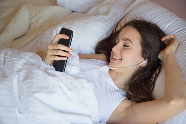 Chica adolescente usando el teléfono celular al despertar se siente feliz por la mañana en la chica de la cama usando el teléfono celular al despertar se siente feliz por la mañana en la cama
 - Foto, imagen