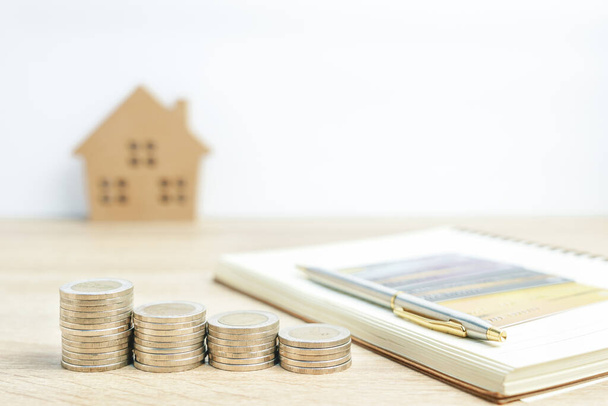 Modelo da casa e bloco de notas com moedas na mesa para o conceito financeiro e bancário
 - Foto, Imagem