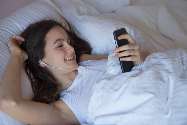 tiener meisje met behulp van mobiele telefoon op wakker voelt zich gelukkig in de ochtend op de beden meisje met behulp van mobiele telefoon op wakker voelt zich gelukkig in de ochtend op het bed - Foto, afbeelding