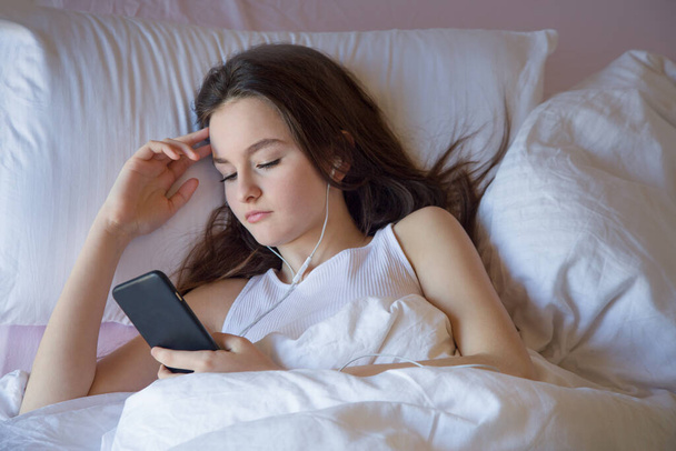 Дівчина-підліток, що використовує мобільний телефон під час пробудження, відчуває себе щасливою вранці на дівчині, яка використовує мобільний телефон під час пробудження, відчуває себе щасливим вранці на ліжку
 - Фото, зображення