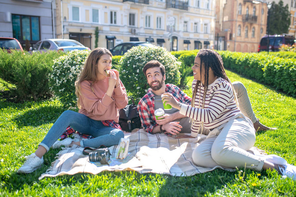 Guy and two girls sitting on plaid on the grass - Photo, Image