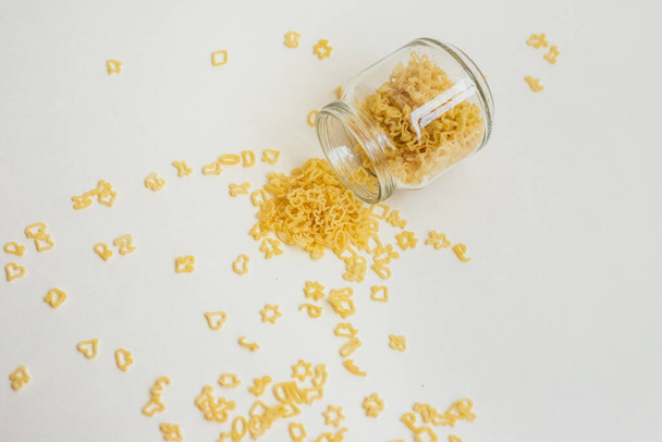 Macaroni in the form of different figures in a glass jar. Small figures made of durum wheat. Children's macaroni. Background and texture of pasta. Space for text. - Fotografie, Obrázek