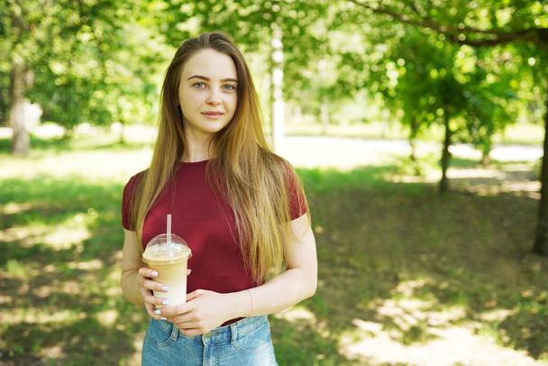 Fiatal vonzó nő elvitelre való itallal séta a parkban. A nő eldobható kávéscsészét tart. Kávét vagy teát. Igyon és egyen a nyári vakáció vagy utazás alatt. Nő hosszú haj és természetes smink. - Fotó, kép