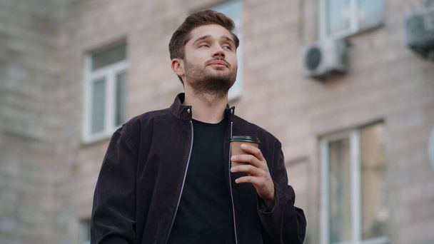 Красивий чоловік п'є каву на вулиці. Позитивний хлопець насолоджується чаєм на відкритому повітрі
. - Фото, зображення
