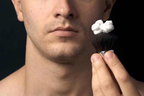 Close-up van een mannelijke kin. Een man brengt scheerschuim aan met een scheerkwast. - Foto, afbeelding