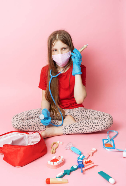 Personal protective equipment: a teenager girl in a medical mask and blue gloves plays a nurse and holds a stethoscope. - Foto, imagen