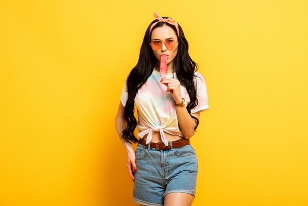 стильна літня брюнетка дівчина їсть морозиво на жовтому фоні
 - Фото, зображення