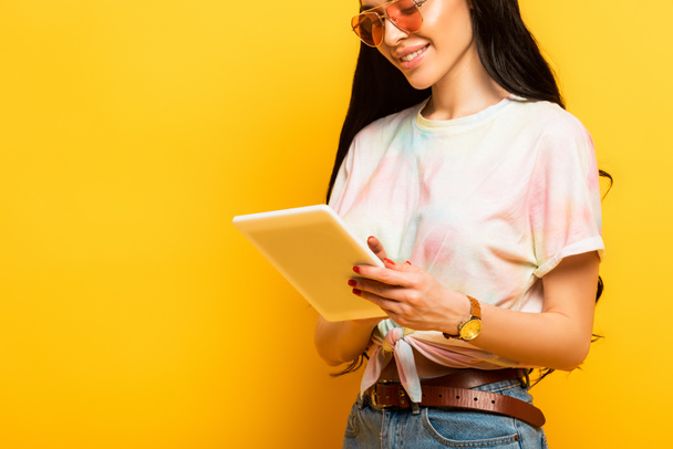 przycięty widok uśmiechnięty stylowy lato brunetka dziewczyna za pomocą cyfrowej tabletki na żółtym tle - Zdjęcie, obraz