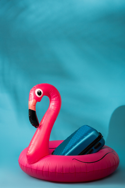 Flamenco y maleta inflable rosa sobre fondo azul
 - Foto, Imagen