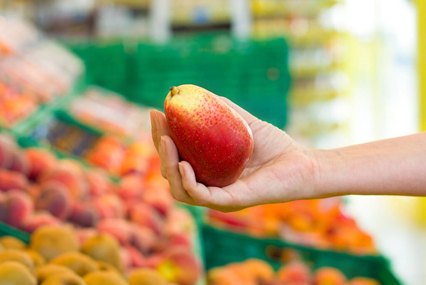 Egy nő mangót választ a szupermarketben. Fogalom az egészséges élelmiszer, bio, vegetáriánus, diéta. - Fotó, kép