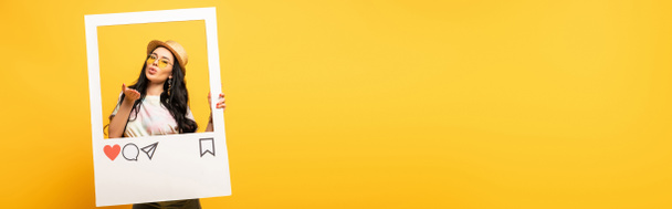 fille brune en tenue d'été posant baiser soufflant dans le cadre du réseau social sur fond jaune, plan panoramique - Photo, image