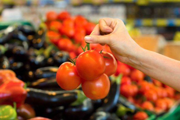 スーパーでトマトを選ぶ女性の手。健康食品、バイオ、ベジタリアン、食事の概念. - 写真・画像