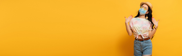 ragazza bruna in abito estivo e maschera medica che soffre di calore su sfondo giallo, colpo panoramico - Foto, immagini