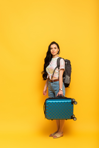 brunette girl with suitcase and backpack on yellow background - Zdjęcie, obraz