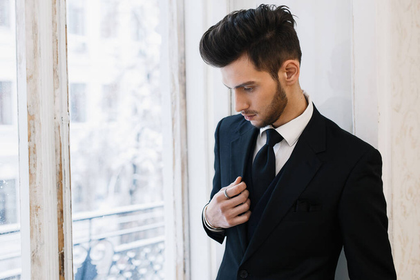 groom in a black suit in a photo studio. posing near the window. elegant wedding - Photo, Image