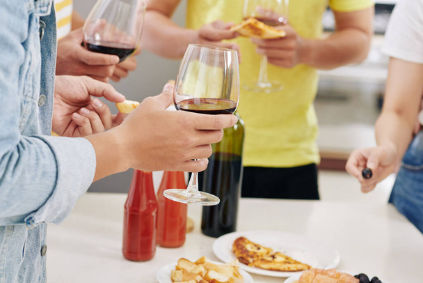 Zugeschnittenes Bild von Freunden, die auf einer Hausparty Rotwein trinken und leckere Pizza essen - Foto, Bild
