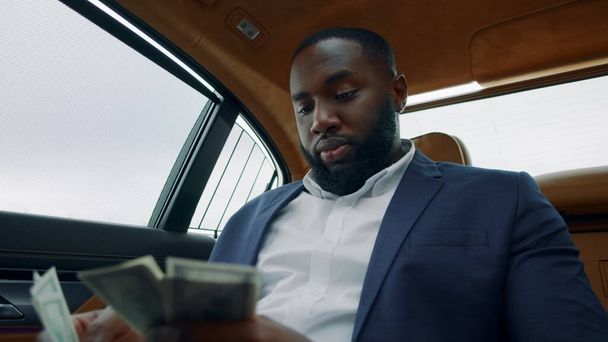 車でお金を数えるビジネスマンの肖像画。アフリカ人の男は車でお金を嗅ぐ - 写真・画像