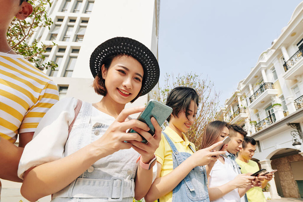 Mulher muito jovem verificando notícias nas mídias sociais ao estar ao ar livre com seus amigos
 - Foto, Imagem