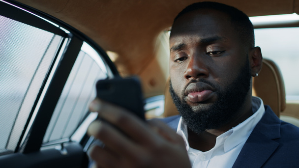 Portré fókuszált afrikai üzletemberről, aki mobiltelefont gépel a hátsó ülésen.. - Fotó, kép