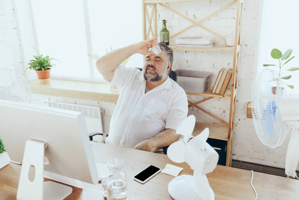 Businessman, manager in office with computer and fan cooling off, feeling hot, flushed - Fotografie, Obrázek