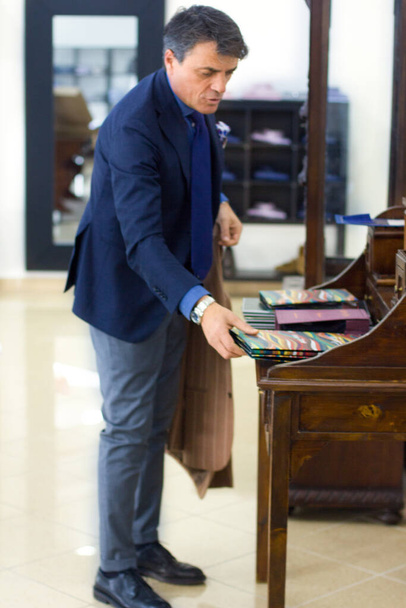 Зрелый профессиональный портной, принимающий мерки для швейного костюма в магазине портных. Человек с измерительной лентой занят. Эксклюзивная ткань на заказ. - Фото, изображение