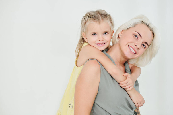 Портрет красивої матері, що носить усміхнену маленьку доньку, ізольовано на світло-сірому
 - Фото, зображення