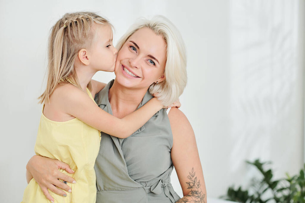 Cute little girl hugging and kissing her smiling mother on cheek - Photo, Image