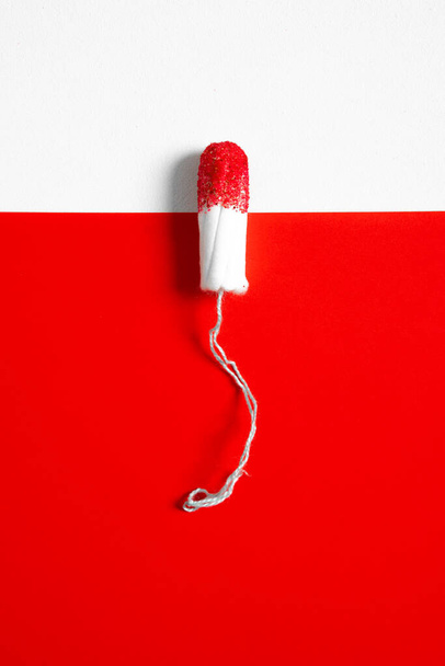 White womens tampon on white and red background and red glitter pigment. Concept photo for womens or feminist blog  - 写真・画像