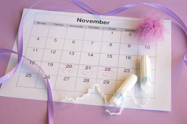Menstrual pads and tampons on menstruation period calendar with on lilac background. - Photo, Image