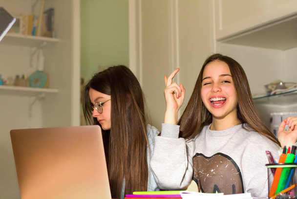 Two teen girls surf the Internet on their laptop, look for products of interest to them and make purchases with a credit card. Teenagers' concept of navigation, research and shopping - Photo, Image