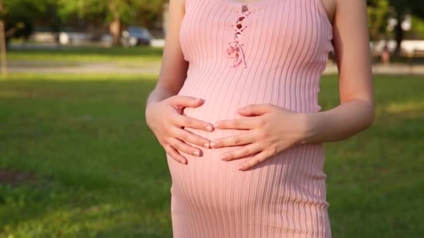 A terhes nő boldogan vigyáz a gyerekére. A fiatal várandós anya terhes hasban tartja a babát az utcán. - Felvétel, videó