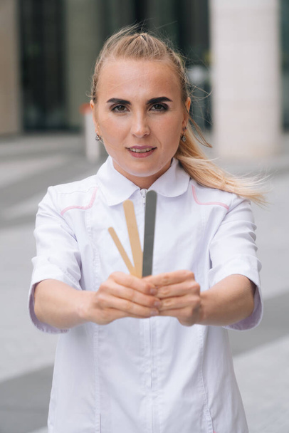 Beautician doctor girl holds a spatula. Woman master of shugaring against the background of a medical clinic - Foto, Imagem