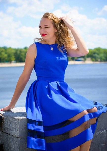 Cabello rubio mujer rizada más tamaño aspecto europeo en azul vestido retro caminar en la ciudad en un día soleado y cálido con buen humor
 - Foto, Imagen