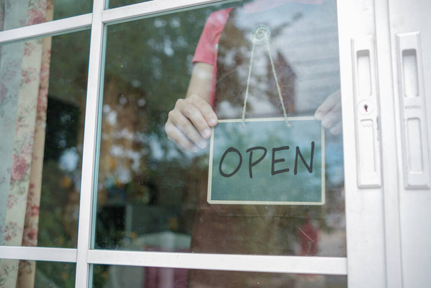 Shop owner show storefront sign hang on the door. It has message tell today is open. - Photo, Image