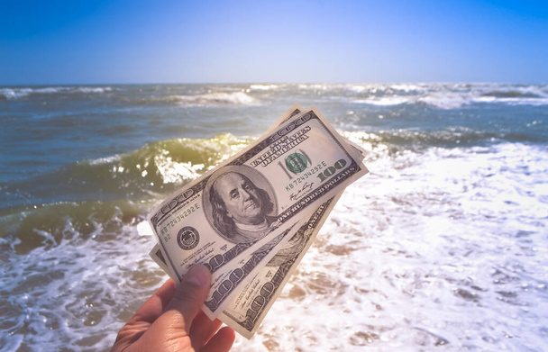 Girl holding a money bill of 300 dollars on background of sea waves - Photo, image