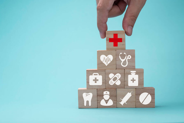 Рука кладе дерев'яні кубики, що укладають медичну допомогу та значок лікарні на синьому фоні. Медичне страхування бізнес та інвестиції
. - Фото, зображення