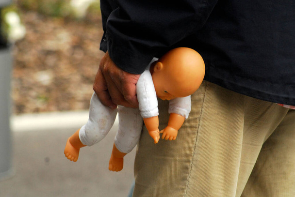 ενήλικο κρατώντας κούκλα μωρό στο ένα χέρι, κακοποίηση παιδιών και βία κατά των παιδιών, εικόνα σύμβολο - Φωτογραφία, εικόνα
