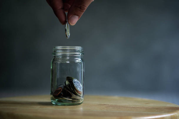 Hand put coin in to glass bottle. Finance, economy concept and saving money concept. - Foto, afbeelding