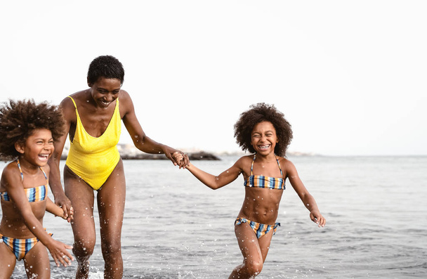 Familia africana feliz corriendo en la playa durante las vacaciones de verano - Afroamericanos divirtiéndose en tiempo de vacaciones - Los padres aman y viajan concepto de estilo de vida - Foto, Imagen