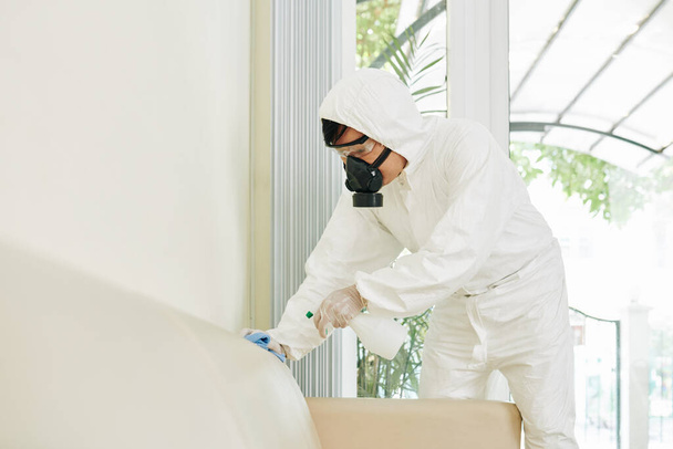 保護スーツの清掃サービス労働者は、抗ウイルスおよび抗菌洗剤で家の中のすべての表面を清掃します - 写真・画像